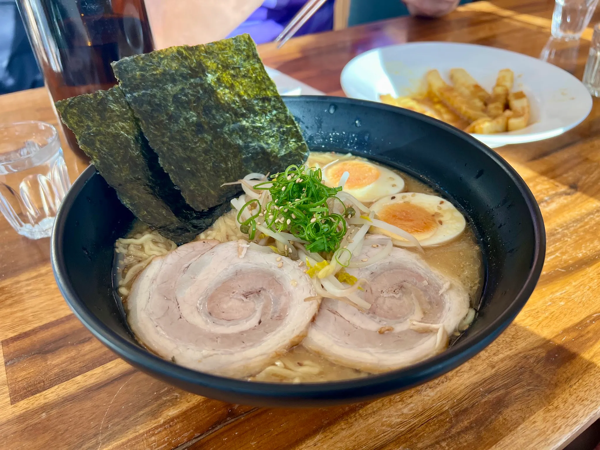 Ramen in matte black bowl with chashu pork rolls, nori and herb garnish