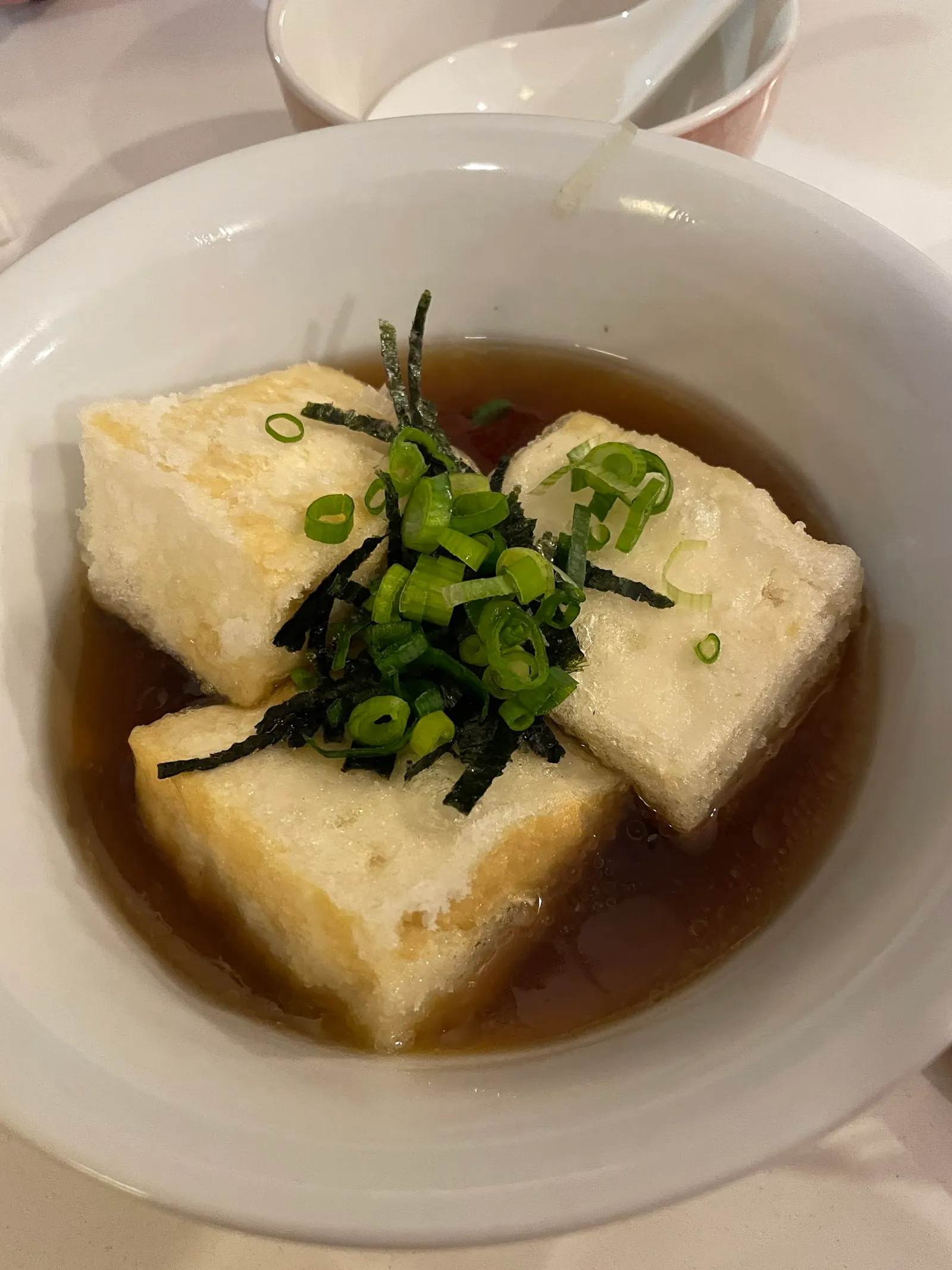 Agedashi tofu with dashi broth, green onion and nori in white bowl